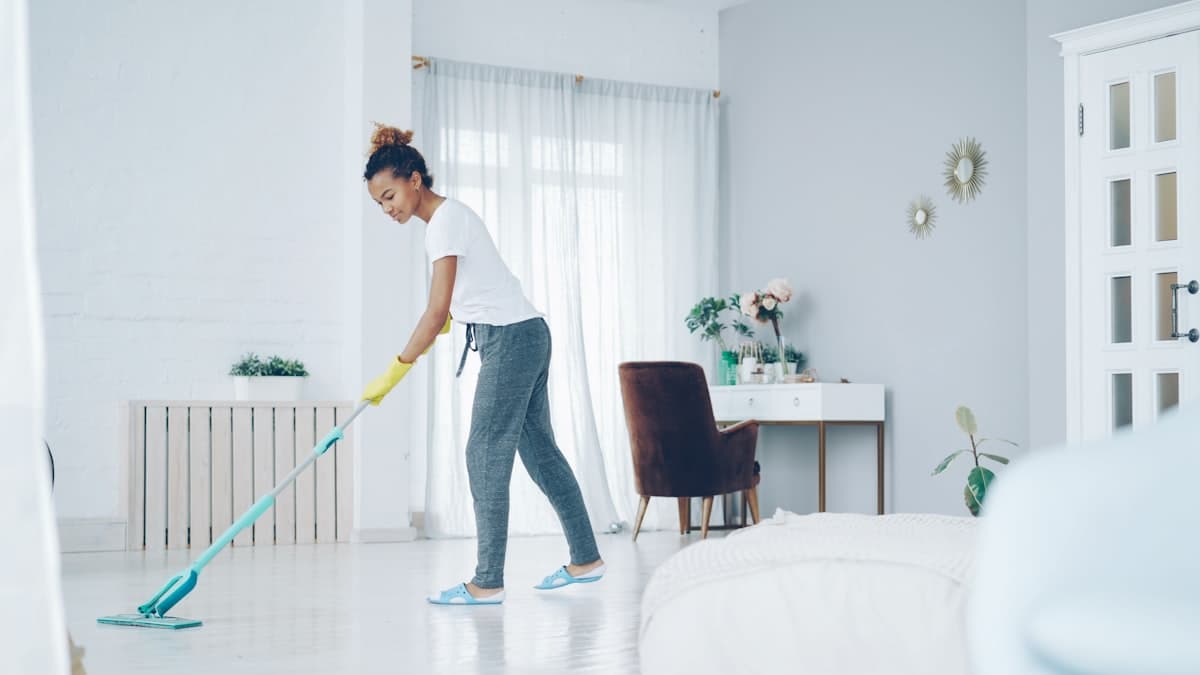 Professional cleaner mopping the floor of a bright, modern Bangkok condo bedroom